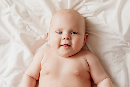 closeup portrait of a blue-eyed newborn baby lying on his back on a white sheet. happy carefree infancy. products for children, natural materials. space for text. High quality photo