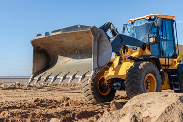 Bulldozer or loader moves the earth at the construction site against the blue sky. An earthmoving machine is leveling the site. Construction heavy equipment for earthworks.