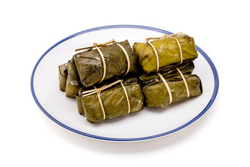 Pile of bundled boiled rice is stacked isolated on white background, Thai dessert made with glutinous rice and coconut milk put banana filling, wrapped in banana leaves and steamed until cooked.