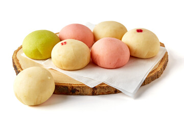 6 pieces of Thai mochi (yellow, pink, green) on a wooden saucer isolated on white background.