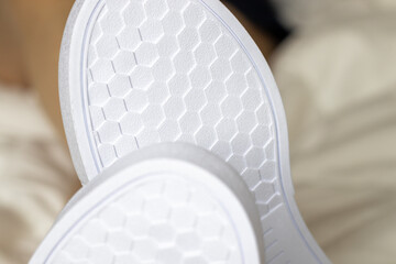 girls legs wearing white color sneakers and sitting in the bed, on white blanket. stay at home concept. stay safe. new sneakers. women is typing a message at the smartphone.