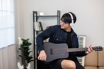 Lifestyle concept. Young asian musician playing guitar in living room at home on this weekend. Relaxing with song and music. Asian man having fun playing acoustic guitar