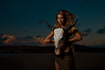 Portrait of woman with long dreadlocks hair hold in hand staff with cow skull with horn against sunset
