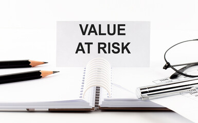 Text VALUE AT RISK on paper card,pen, pencils, glasses,financial documentation on table - business concept