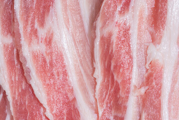 Close up top view pack bacon, pieces raw meat of fresh red pork with white fat slices are sliced into thin strips stacked on top of each other
