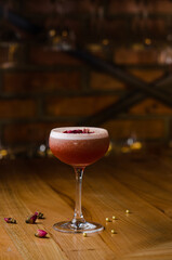 Classic cocktail glass on a wooden table in a nightclub restaurant. Alcoholic cocktail of pink color with a rose, close-up. Modern alcoholic drink