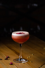 Classic cocktail glass on a wooden table in a nightclub restaurant. Alcoholic cocktail of pink color with a rose, close-up. Modern alcoholic drink