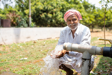 Happy Indian farmer after seeing water on borewell pipe at farmland - concept of happiness, poverty and water for agricultural works