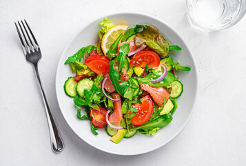 Salad with salmon, vegetables, herbs and flax and sesame seeds on a light gray background.