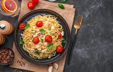Popular pasta with feta cheese, cherry tomatoes and garlic on a dark background.