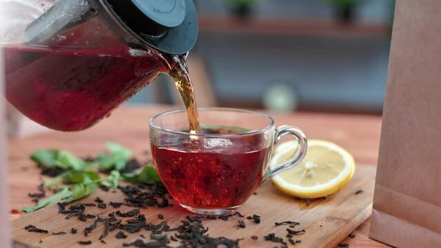 Black fragrance natural tea pouring from teapot into transparent glass on wooden table