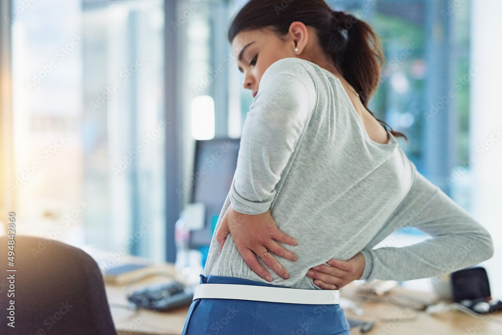 Poster whats this sharp sting in my back. shot of a young businesswoman suffering from back pain while work