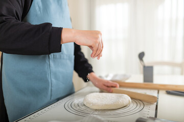 Chef in apron sprinkles flour on cooked wheat pastry dough on silicone baking mat. Selective focus, copy space.