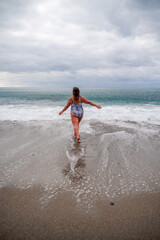 A plump woman in a bathing suit enters the water during the surf. Alone on the beach, Gray sky in the clouds, swimming in winter.