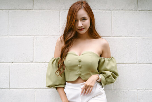 Portrait of sexy young Asian woman wear green off-shoulders clothes and looking at camera standing against white brick wall. Fashion look , beauty and style.