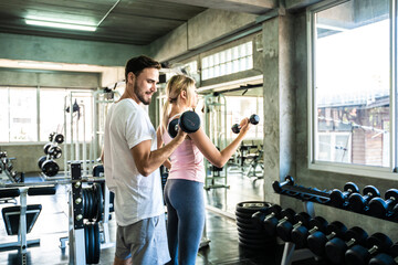 Couple lifting dumbbell in fitness gym man couching women in sport gym