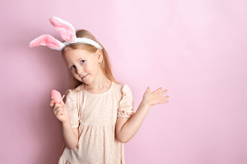 Obraz na płótnie Canvas Happy Easter. A cute girl with rabbit ears holds colored eggs in her hands and smiles cheerfully. pink background. Space for text.
