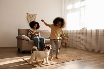 Two beautiful black girls of different age playing with their adorable wire haired Jack Russel terrier puppy at home. Loving sisters with rough coated pup having fun. Background, close up, copy space.