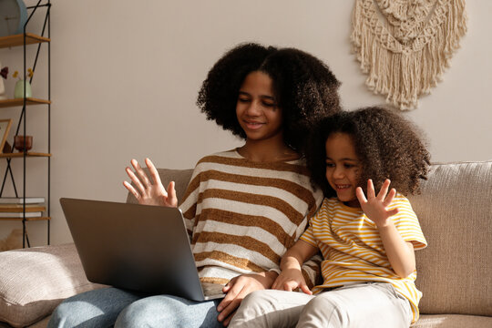 Two beautiful black girls of different age on a video call at home. Loving sisters sitting together on the couch with laptop. Background, close up, copy space. - Powered by Adobe