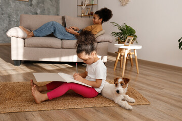 Two beautiful black girls of different age playing with their adorable wire haired Jack Russel terrier puppy at home. Loving sisters with rough coated pup having fun. Background, close up, copy space.