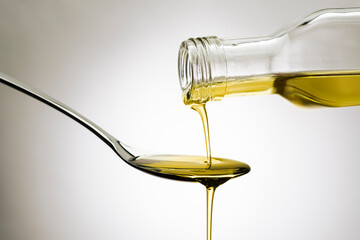 Olive oil bottle pouring oil on spoon, on gradient background