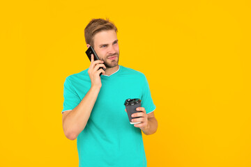 man in shirt speaking on smartphone with morning coffee on yellow background, phone call