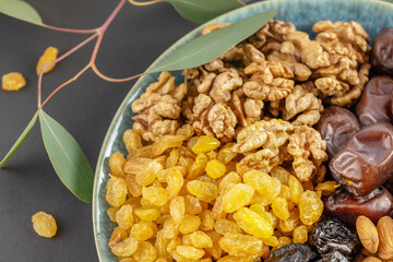 Golden raisins, walnuts, almonds, prunes and dates in the blue bowl on a black background with a twig with green leaves. Arabian dish with nuts and dried fruits. Healthy vegan food