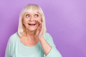 Photo of excited old lady palm open mouth share secret look empty space wear blue shirt isolated...
