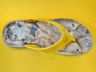 Broken and wasted children flip flops on yellow studio background top view