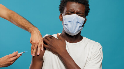 Scared person with face mask getting vaccinated against coronavirus. Hands of doctor with syringe...
