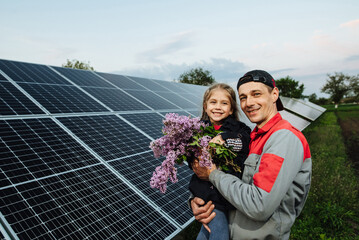 The child hugs the dad the electrician, on a background of solar panels. The engineer shows the girl the future of alternative energy and sustainable energy. The concept of ecology, a happy future.