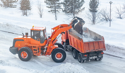 Big orange tractor cleans up snow from the road and loads it into the truck. Cleaning and cleaning...
