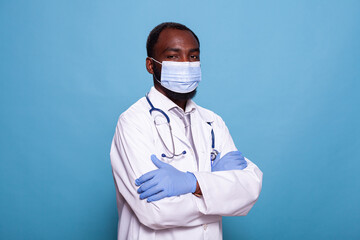 Portrait of confident doctor wearing scrubs with face mask and latex gloves before consult. Medic with stethoscope wearing protective medical gear and white lab coat.