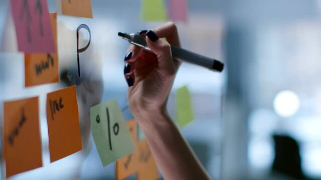 Cropped shot of female hand writing PLAN on glass board with colorful stickers in modern office