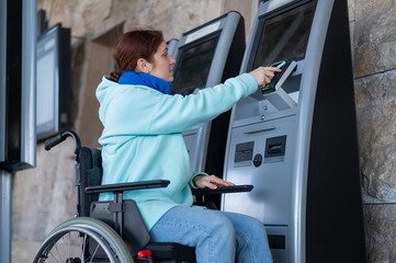 Caucasian woman in a wheelchair buys a train ticket using a mobile phone at a self-service...