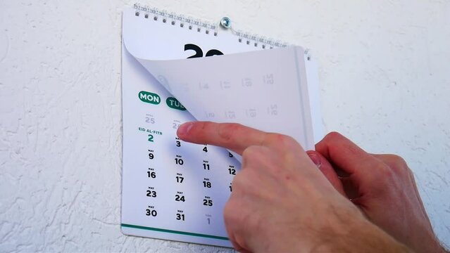 Male hands turns the wall calendar April page 2022 and points a finger at Eid al-Fitr date on the next one