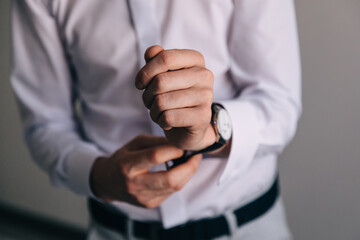 The man fastens a cufflink on his shirt. The groom is getting ready for the wedding ceremony.