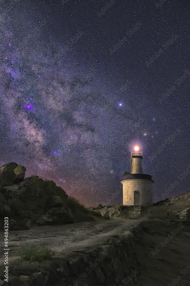 Aufkleber vertical shot of an illuminated lighthouse placed on a shore in the background of a starry sky.