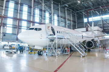 White passenger airplane in the hangar. Airliner under maintenance. Checking mechanical systems for...