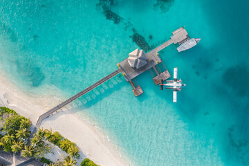 Beautiful aerial view of Maldives jetty seaplane top view with wooden boat and tropical beach. Luxury tropical resort or hotel with water villas and beautiful beach scenery. Amazing bird eyes view - obrazy, fototapety, plakaty