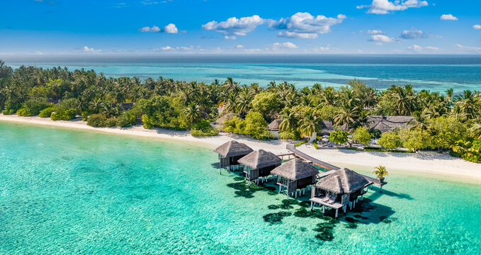Aerial view of Maldives island, luxury water villas resort and wooden pier. Beautiful sky and ocean lagoon beach background. Summer vacation holiday and travel concept. Paradise aerial landscape pano
