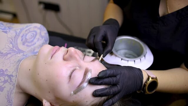 after the procedure of permanent eyebrow makeup, the master performs the waxing procedure applies wax to remove hairs to the contour of the eyebrows.