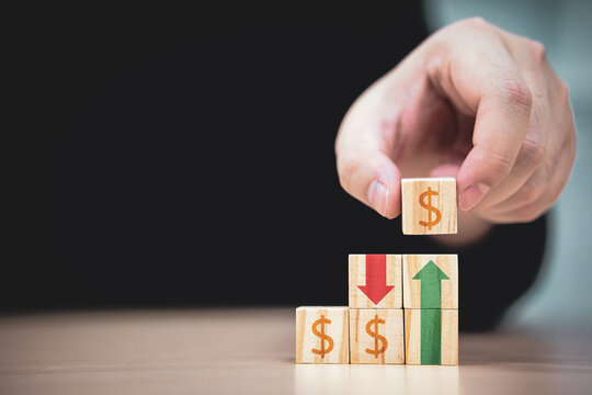 risk of currency exchange rates. The increase and decrease of profit from business results. man's hand picked up wooden block with the dollar sign and placed it on wooden block.