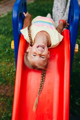 Funny little girl playing on a slide at a playground. Childhood. Summertime