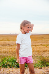 Smiling little girl in white t-shirts standing in field outdoor. Mock up.