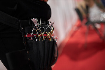 a black hairdresser's bag with sharp metal scissors hanging from her waist. hairdressing scissors...