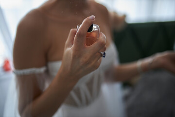 The bride is holding a perfume. the bride has the final preparation for the wedding. Bride in delicate elegant dress applying perfume on her wrist closeup - Powered by Adobe