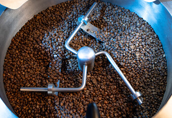 Production of freshly roasted coffee beans. Industrial mixing machine for mixes roasted coffee beans in roaster, close up. Roasting process. Food and drink background for cafe.