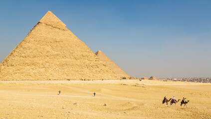 The great Pyramid complex of Giza with tourists riding camels in front of the Egyptian pyramids....