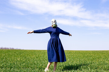 Gas mask on the face of a young girl. A young girl in the middle of a green field.